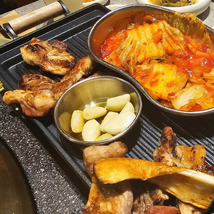 육화미 천안본점 불판에서 구운 돼지고기와 새송이버섯, 옆 팬에 담긴 구운 김치와 마늘기름