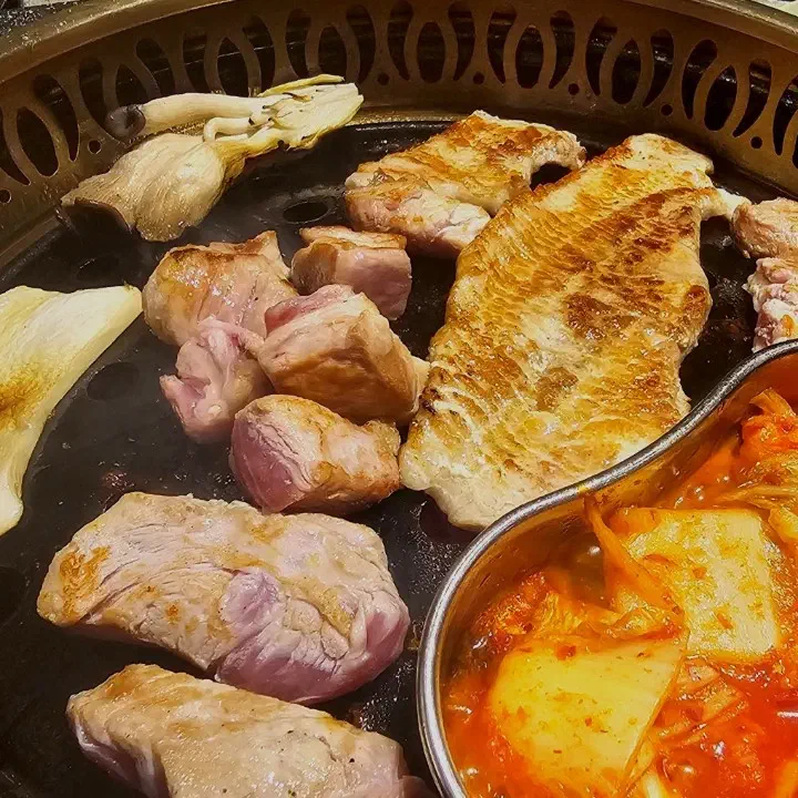 육화미 천안본점 원형 불판에 구운 숙성 삼겹살과 목살, 버섯, 옆 팬에서 함께 익는 김치