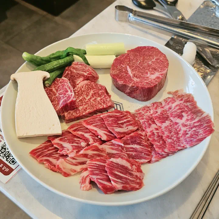 육화미 천안본점에서 나온 생 소고기 모둠 접시, 마블링이 뚜렷한 여러 부위가 새송이버섯·꽈리고추와 함께 흰 접시에 담겨 있다