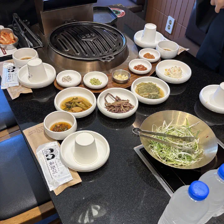 육화미 천안본점 테이블 위에 불판과 여러 밑반찬 그릇, 파채가 차려진 모습