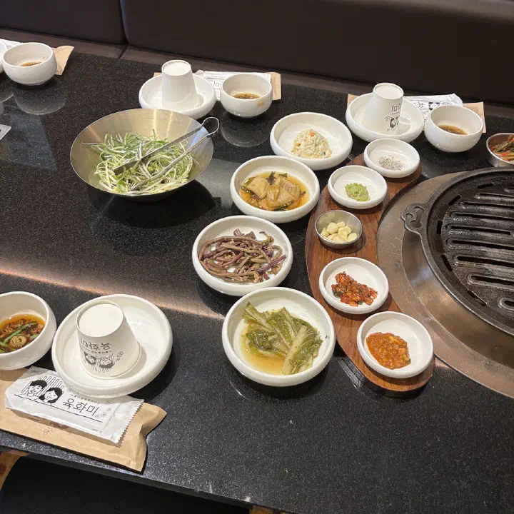 육화미 천안본점 고깃집 테이블에 밑반찬 여러 종류와 숯불 그릴이 차려진 모습