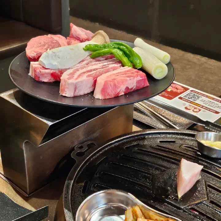 육화미 천안본점 테이블에 생삼겹살과 목살 등 생고기 접시가 채소와 함께 놓인 모습