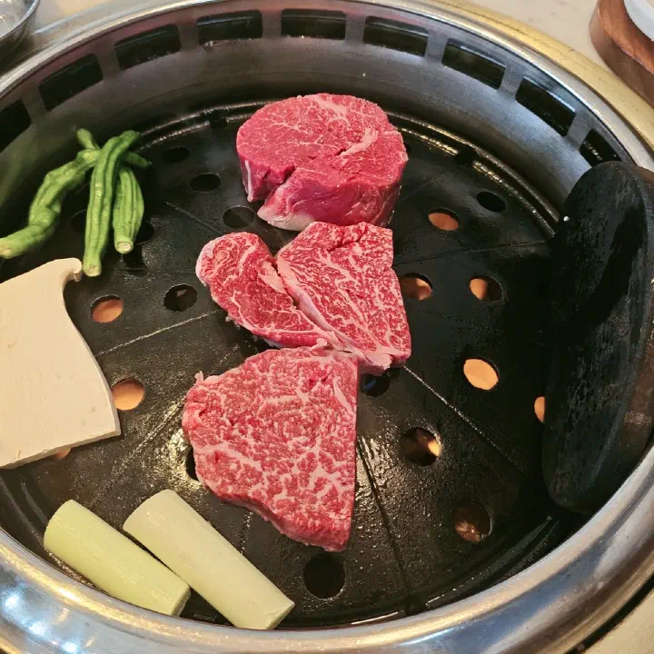 육화미 천안본점 원형 불판에 올린 마블링 선명한 소고기와 꽈리고추, 대파, 새송이버섯
