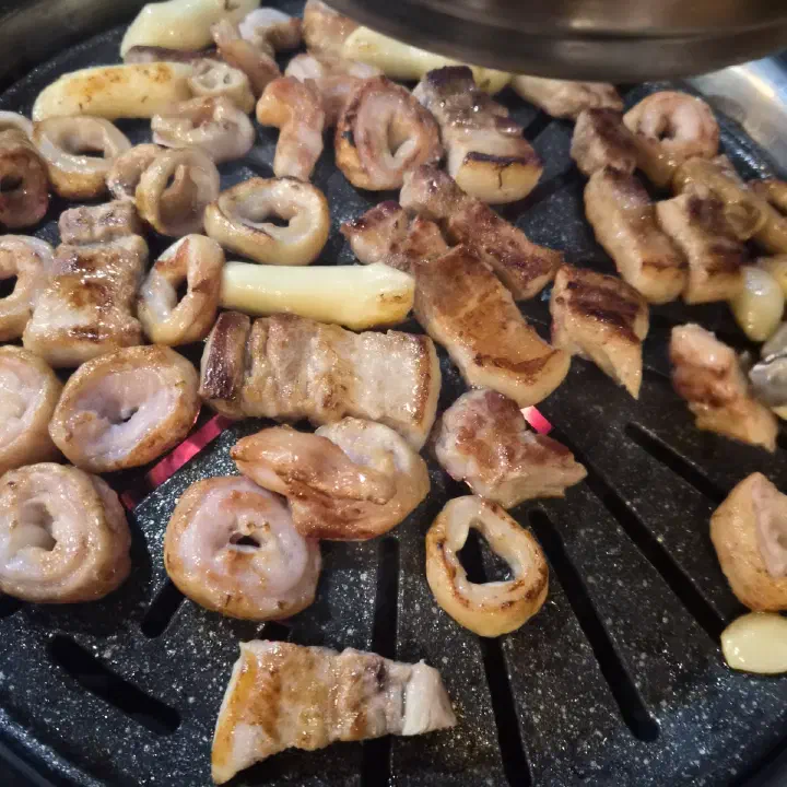 아리조나막창 숯불 불판 위 생막창과 생삼겹살, 떡·마늘