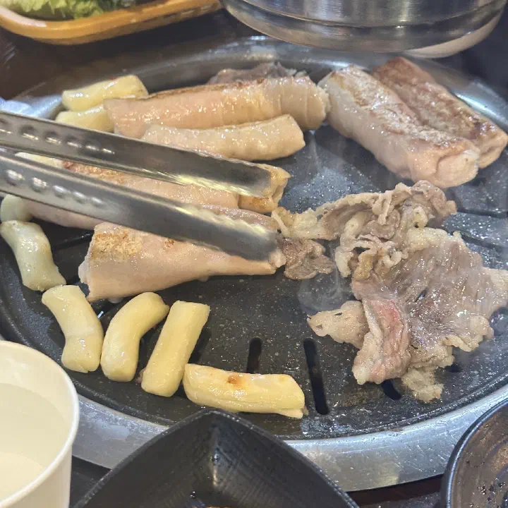 아리조나막창 불판 위 두툼한 생삼겹살과 떡, 얇게 썬 고기