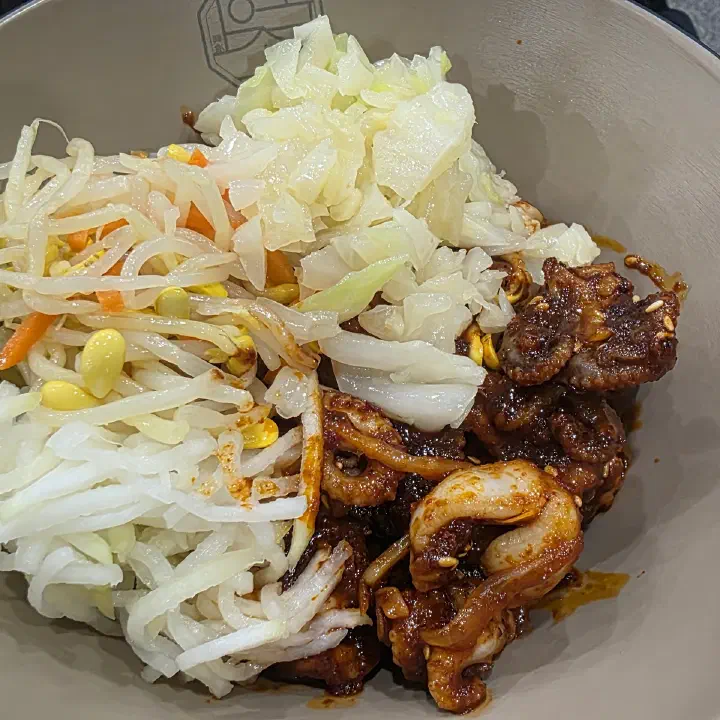 손의손 본점에서 나온 갈색 양념에 버무린 족발 또는 발 부위 요리 한 그릇을 위에서 찍은 사진, 옆에 절인 채소가 곁들여져 있다