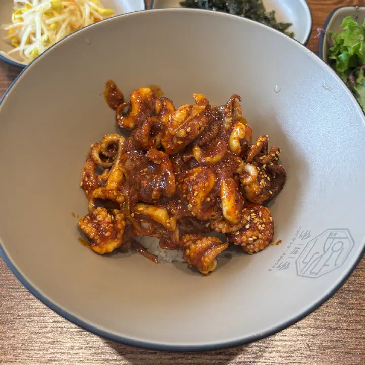손의손 본점에서 나온 매콤한 양념 낙지볶음 덮밥을 가까이서 찍은 사진으로, 깨가 뿌려진 낙지가 밥 위에 수북이 올라 있다.