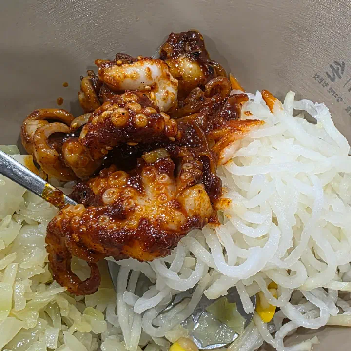 손의손에서 나온 매콤한 양념 연체동물 볶음이 채 썬 무와 양배추 위에 올려진 클로즈업 사진