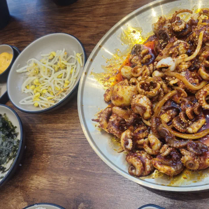 손의손 본점에서 나온 매콤한 양념에 볶은 낙지 요리가 은색 둥근 접시에 가득 담겨 있고, 옆에 숙주나물과 김가루 반찬이 놓인 모습