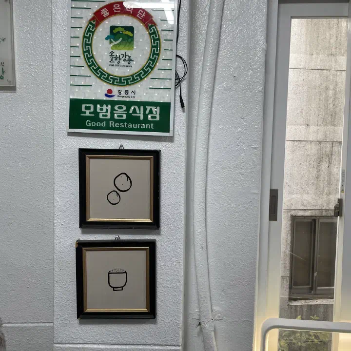 감자바우 입구 벽에 걸린 강릉시 모범음식점 인증판과 감자 그림 액자