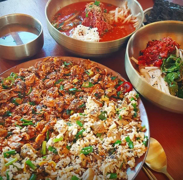 향화정 홀 나무 테이블에 차려진 꼬막무침비빔밥과 육회물회, 육회비빔밥