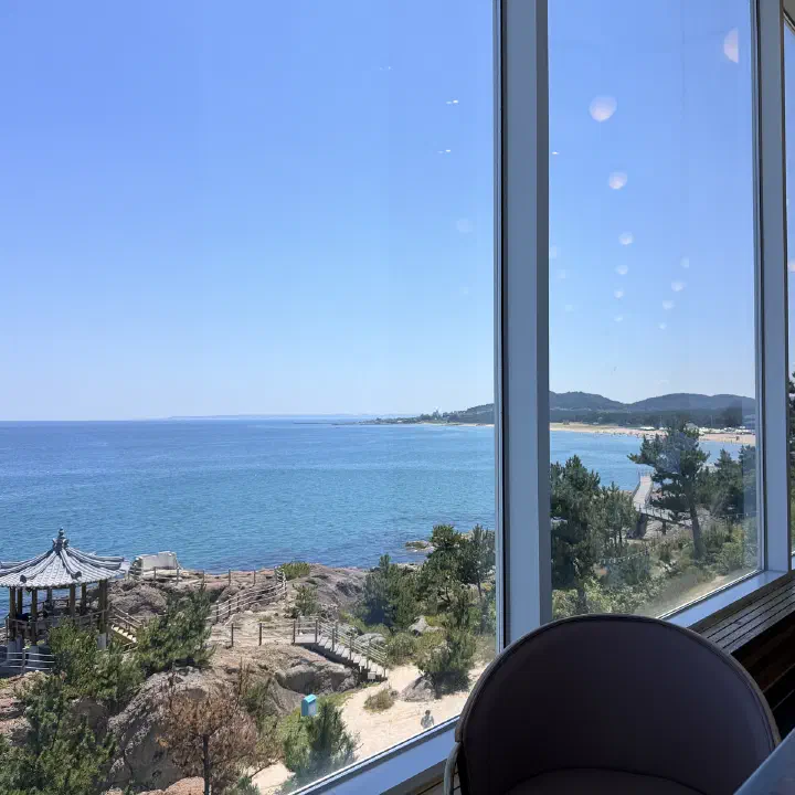 러블랑 통창 너머 동해와 바위 위 정자, 창을 향해 놓인 의자