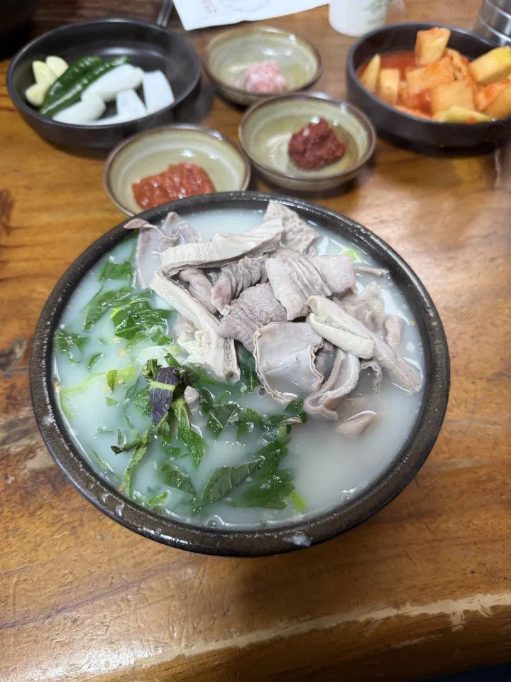 충남식당 국밥과 깍두기, 새우젓, 다대기, 양파 등 반찬을 차린 나무 테이블 상차림