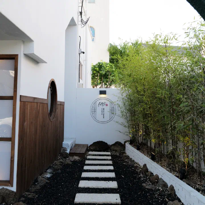 서리단 외부 디딤돌 길, 흰 담장의 원형 로고와 대나무 화단