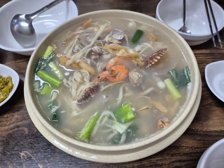 해물칼국수 한 대접과 청양고추 장아찌 등 반찬 그릇이 함께 놓인 상차림