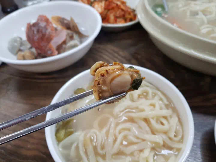 황해해물칼국수에서 추가 주문한 전복을 젓가락으로 집어 든 모습