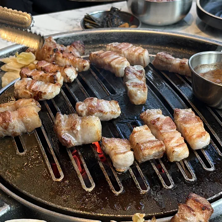 숙성도 중문점 원형 불판 위에서 노릇하게 구워지는 삼겹살 고기 조각 근접 사진