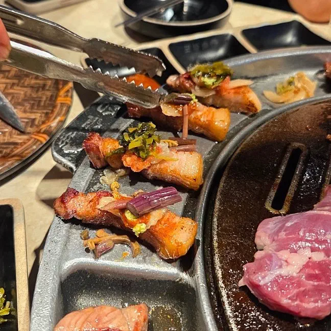 숙성도 중문점 불판 옆 경사진 판 위에서 집게로 구운 삼겹살 고기를 집은 모습