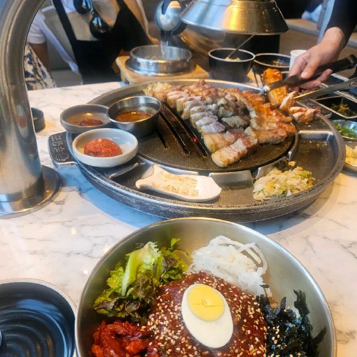 숙성도 중문점 테이블 위 불판에서 구워지는 삼겹살과 앞쪽에 놓인 비빔 요리 그릇
