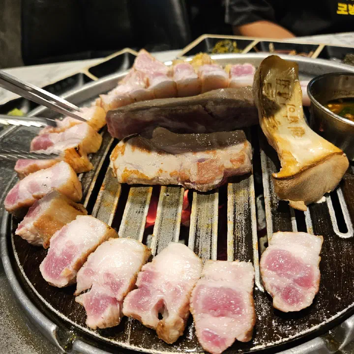 숙성도 중문점 불판 위에서 숙성 돼지고기 조각과 큰 버섯이 집게와 함께 구워지는 모습