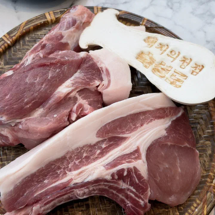 숙성도 중문점의 대나무 소쿠리 위에 놓인 생돼지고기 두 덩이와 글자가 새겨진 버섯 모양 나무 팻말
