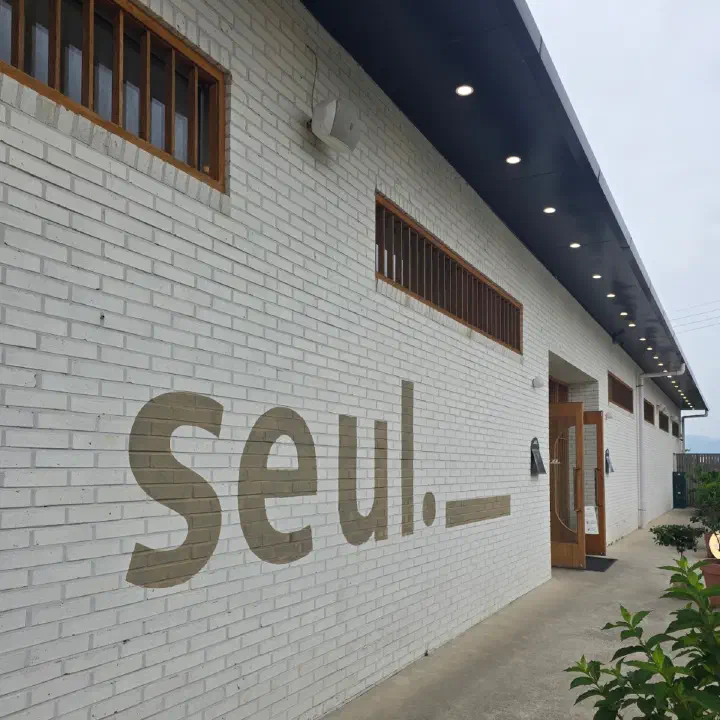 슬지제빵소 흰 벽돌 외벽의 seul 레터링과 나무문 출입구
