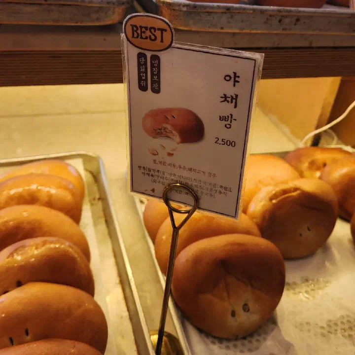 이성당 매대에 야채빵 설명과 2,500원 가격표가 놓이고 주변에 갈색 빵들이 쌓여 있다