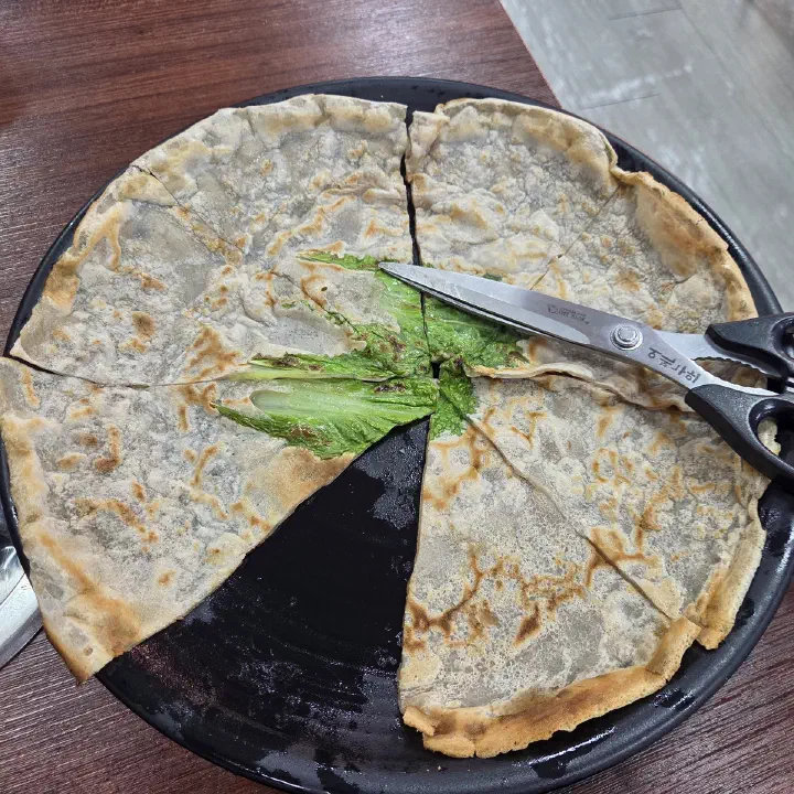 감동식당에서 부추전으로 보이는 전을 가위로 잘라 나눠 먹기 좋게 손질한 모습이다