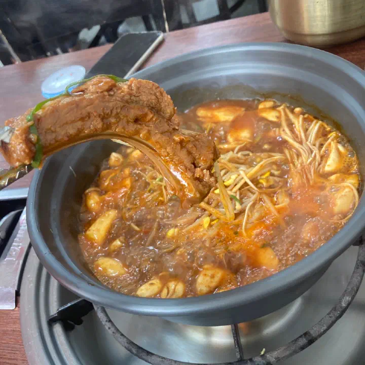 감동식당 노원본점의 매콤한 갈비찜 냄비에서 갈비 한 대를 집게로 들어 올리는 모습이다.