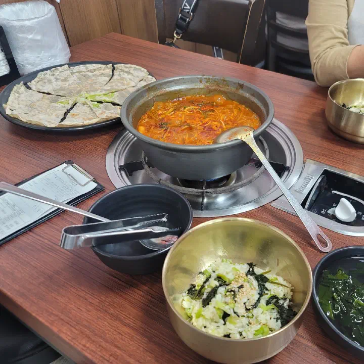 감동식당 노원본점 테이블에 김치찌개 냄비와 파전, 돌솥 나물밥, 반찬이 차려져 있다.