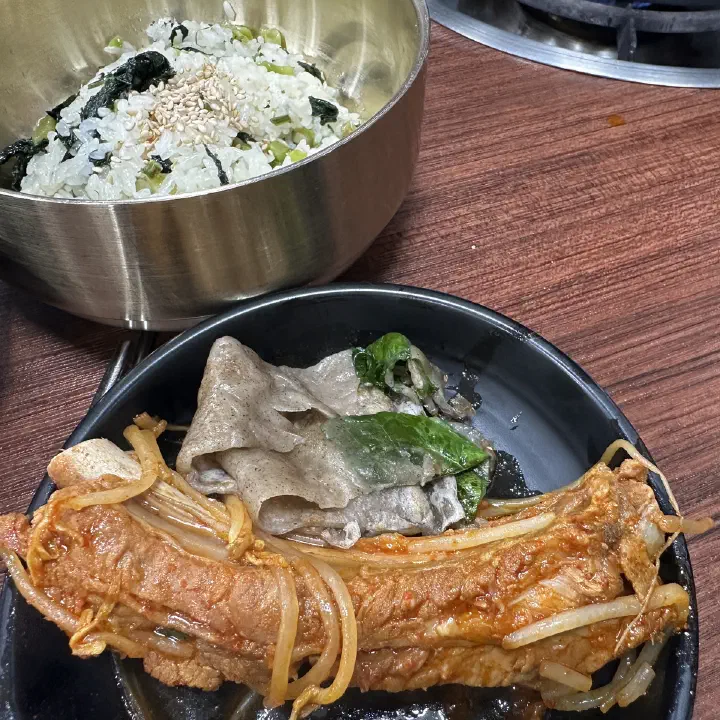 감동식당 노원본점에서 매콤하게 양념된 돼지갈비와 메밀전병, 양념 나물이 담긴 검은 접시와 나물솥밥이 놓인 모습