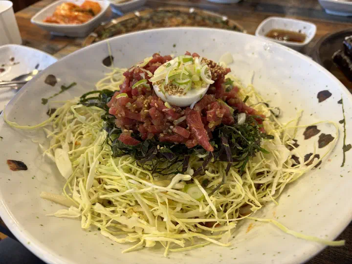 채 썬 양배추와 깻잎 위에 육회가 올라간 나사리식당 육회비빔칼국수